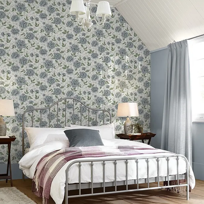 Laura Ashley Vliestapete Pickworth - Hellblau, Floral, 1.000 x 52 cm - Graues Metallbettgestell mit weißer Bettwäsche und gestreifter Decke in einem Schlafzimmer.