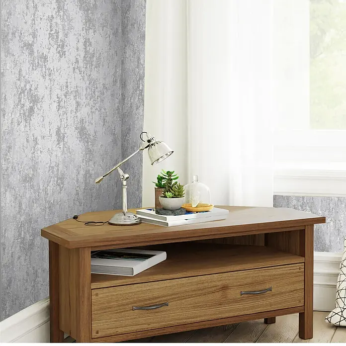 Laura Ashley Vliestapete Whinfell - Silber, Uni, 1.000 x 52 cm - Eck-Holztisch mit Schublade und offenem Fach, dekoriert mit Lampe und Pflanzen. Mittleres Braunholz.