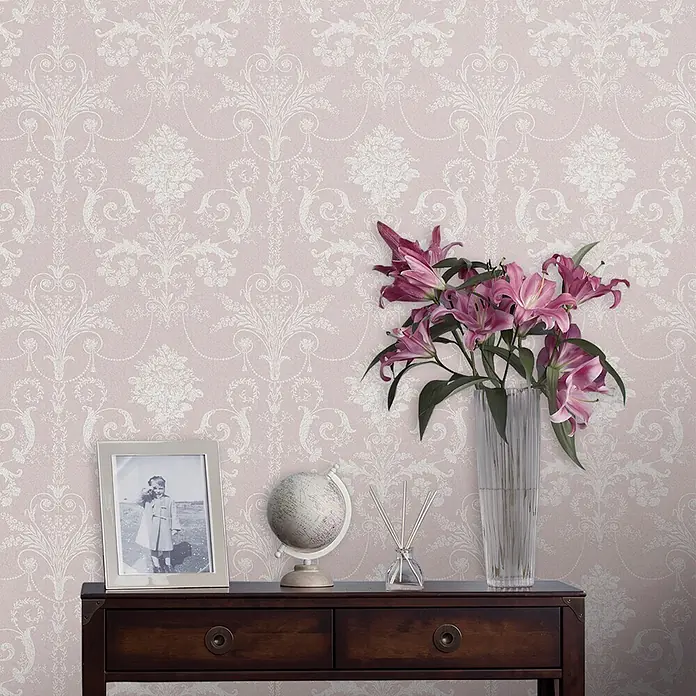 Laura Ashley Vliestapete Vliestapete Josette Damast - Amethyst/Rosa, Ornament - Elegante Damasttapete in Hellrosa mit weißen Zierleisten, an einer Wand hinter einem Dekorationstisch.