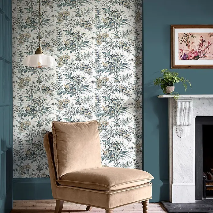 Laura Ashley Vliestapete antikes Textil - Beige, Floral, 1.000 x 52 cm - Blaue, grüne und beige Blumentapete schmückt eine Wand, ergänzt durch eine tealfarbene Wand und einen cremefarbenen Sessel.