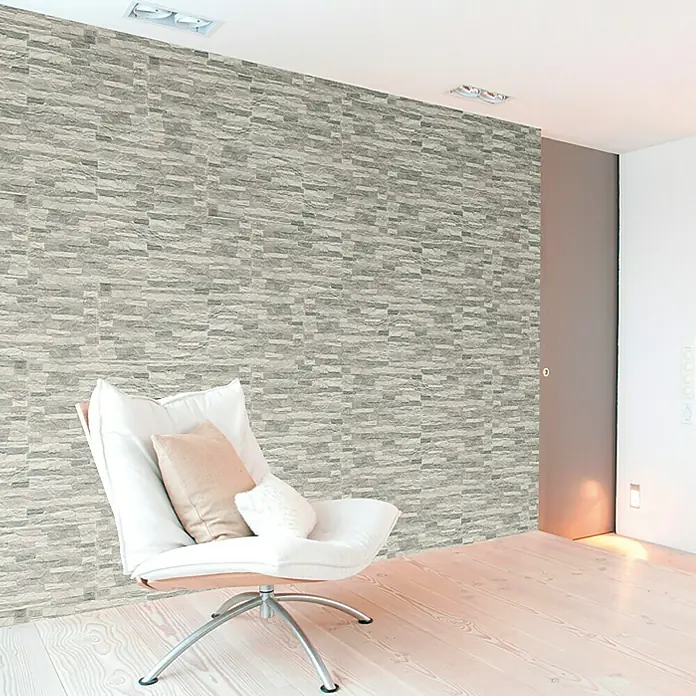 Verblendstein Aitana Gris - 50 x 33,5 cm, Grau, Steinoptik - Gemütlicher Sessel mit Kissen in modernem Raum mit Steinwand und Holzboden. Perfekt zum Entspannen und Genießen des Ambientes.