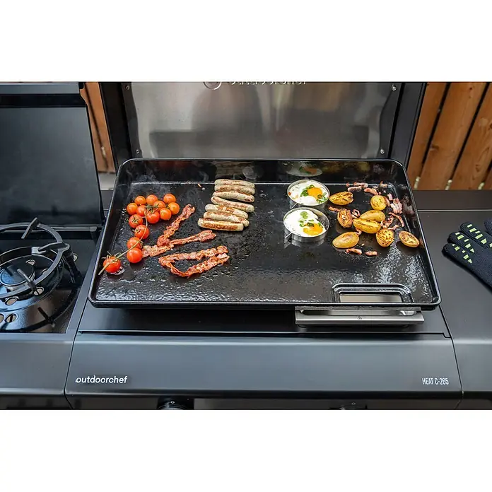 Outdoorchef Plancha-Grill Heat C265 - Grillfläche (B x T): 62 x 37 cm, 7,2 kW, Anzahl Brenner: 2 Stk., Schwarz - Schwarze Bratplatte auf einem Outdoorchef-Grill, brät Würstchen, Speck, Tomaten, Spiegeleier und Kartoffeln.