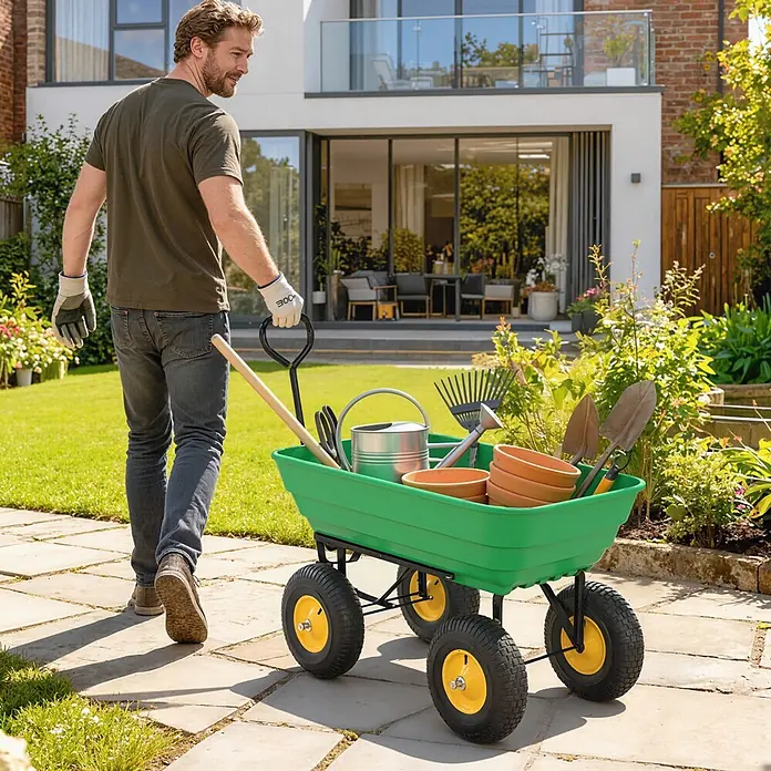 Outsunny Bollerwagen - Traglast: 200 kg, Stahl - Mann zieht einen grünen Gartentrolley mit gelben Rädern, gefüllt mit Gartengeräten und Terrakotta-Töpfen, über einen Gartenweg.