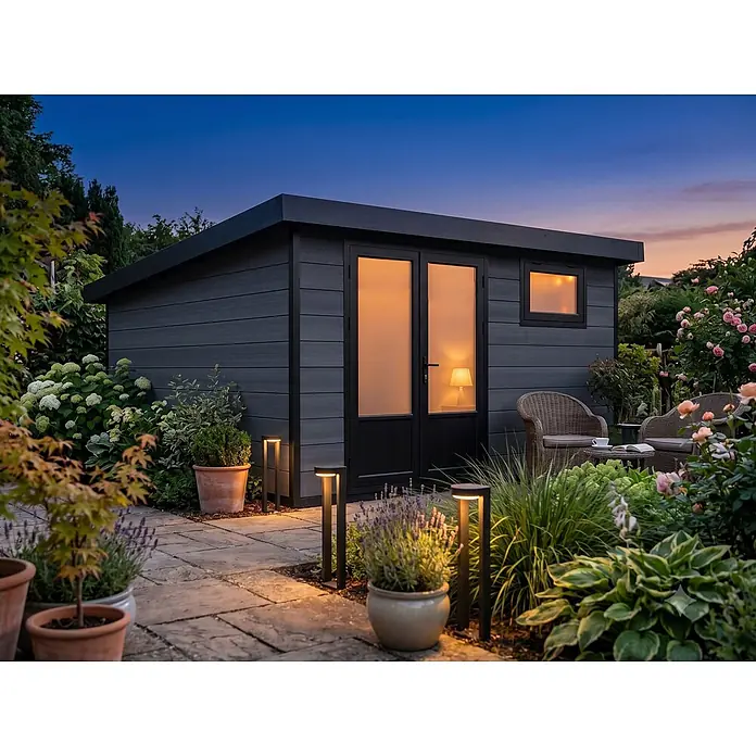 Fjordholz Gartenhaus Style DeLuxe 13,70 m² - Außenmaß inkl. Dachüberstand (B x T): 408 x 405 cm, Aluminium, Anthrazit/grau - Dunkelgraues, modernes Gartenhaus/Büro mit leuchtenden Innenlichtern in der Dämmerung, umgeben von Pflanzen und Gartenmöbeln.