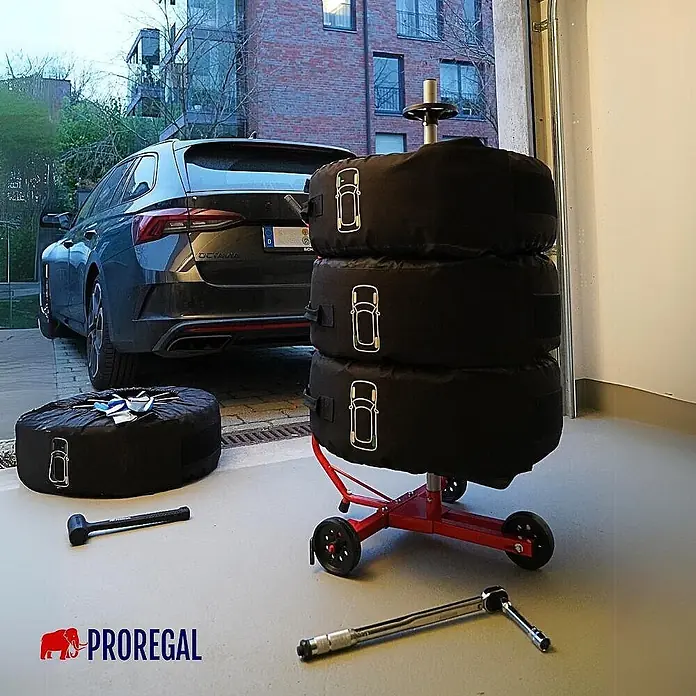 Proregal Reifenregal Fahrbarer Felgenbaum CARRERO - Stecken, Rot - Schwarze Reifenabdeckungen auf rotem mobilen Reifenständer, zusätzlicher Reifen und Werkzeug auf Garagenboden neben Auto.