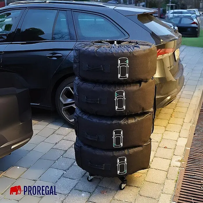 Proregal Reifenregal Fahrbarer Felgenbaum CARRERO - Stecken, Schwarz - Stapel von vier schwarzen Reifen-Tragetaschen auf einem Rollwagen neben einem Auto. Jede Tasche zeigt ein Auto-Diagramm für den organisierten Reifentransport.