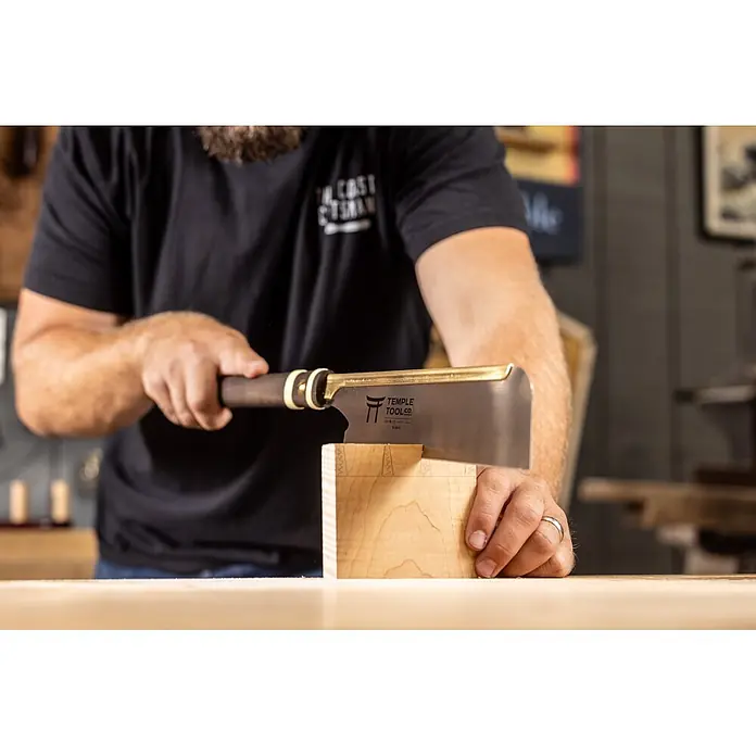 Temple Tool Japansäge Dozuki Rip Cut - Blattlänge: 240 mm - Eine Person verwendet eine japanische Zugsäge mit Messingrücken und dunklem Griff, um ein Stück Holz zu sägen.