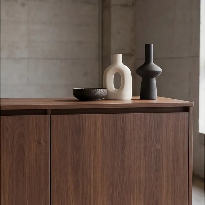 Happy Garden Kommode SARAH - Dunkles Holz - Dunkler Holzschrank mit einer hellbeigen Vase mit offener Form, einer schwarzen Skulpturvase und einer dunklen strukturierten Schale auf seiner Oberfläche.
