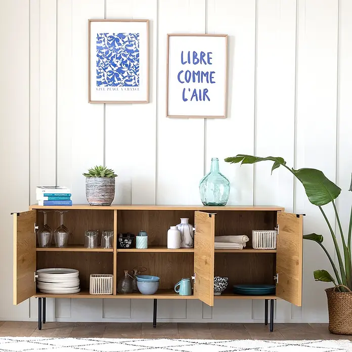 Happy Garden Kommode STINNA - Natürlich - Helles Sideboard aus Eiche mit schwarzen Beinen, offenen Regalen und geschlossenen Schränken, dekoriert mit Geschirr und Dekoartikeln.