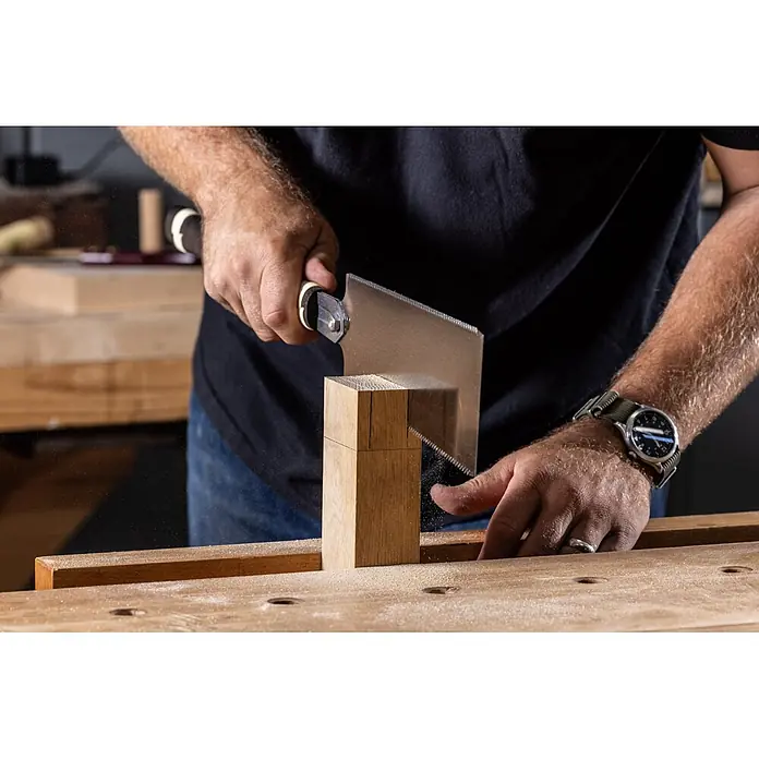 Temple Tool Japansäge Ryoba - Blattlänge: 240 mm - Ein Schreiner benutzt eine japanische Zugsäge, um helles Holz präzise zu schneiden, wobei feiner Sägemehl auf einer Werkbank entsteht.