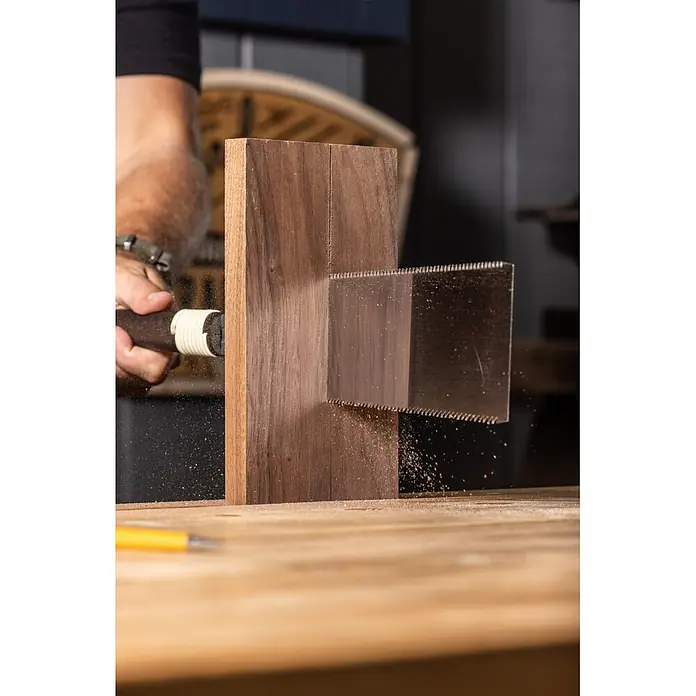 Temple Tool Japansäge Ryoba - Blattlänge: 240 mm - Eine Handsäge mit dunklem Griff und Metallblatt schneidet einen dicken Holzklotz. Feiner Sägemehl fliegt, während eine Hand die Säge führt.