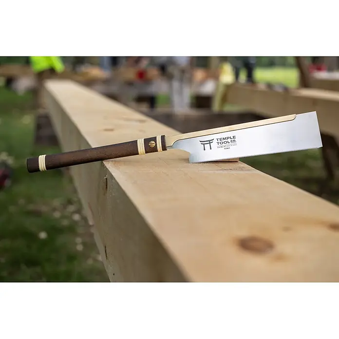 Temple Tool Japansäge Dozuki Cross Cut - Blattlänge: 240 mm - Eine japanische Zugsäge mit dunklem Holzgriff und Messingdetails liegt auf einem hellen Holzbalken.