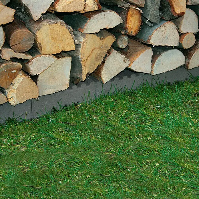 Christoph Fundamentstein - 22 x 22 x 8 cm, Beton - Holzstapel auf Steinen. Das Holz ist gespalten und gestapelt. Der Hintergrund ist Gras. Das Holz ist für den Winter vorbereitet.