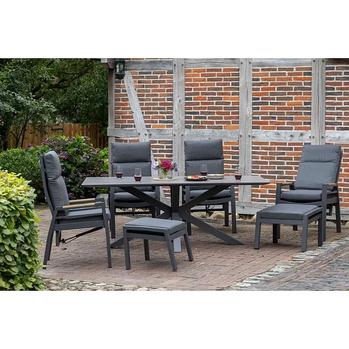 Bene Living Gartentisch-Set Sevilla + Hocker mit Tisch Sevilla - Gesamtumfang: 7 -tlg., Aluminium pulverbeschichtet, Textilene, Keramik, Ausziehbar - Dunkelgraues Aluminium-Outdoor-Essgruppe mit gepolsterten Stühlen und Ottomane auf einer Ziegelterrasse, für eine Mahlzeit gedeckt.