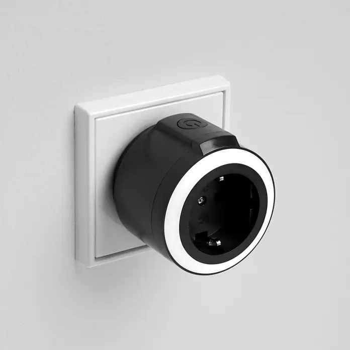 REV Funkschalter Set 2+1, Comfort -  - Schwarzer Smart-Stecker mit weißem LED-Ring und Power-Taste, eingesteckt in eine weiße Wandsteckdose.