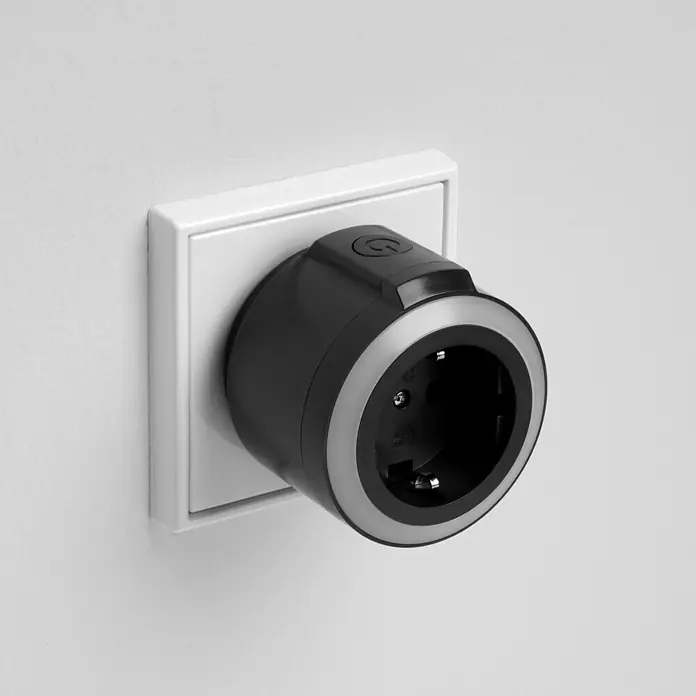 REV Funkschalter Set 2+1, Comfort -  - Schwarz-grauer Smart-Steckdosenadapter mit Power-Taste, in eine Wandsteckdose gesteckt.