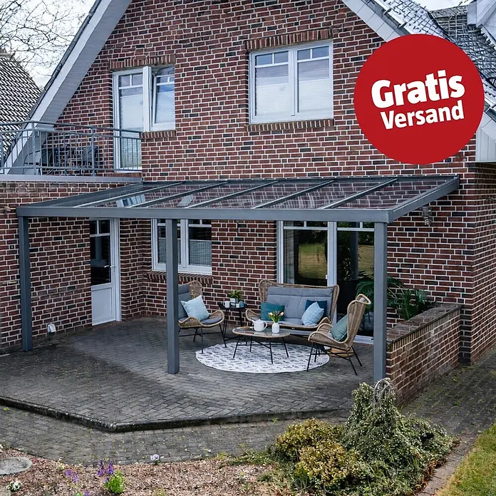 Gardendreams Terrassenüberdachung Elegance - B x T: 600 x 405,5 cm, Graualuminium, Verbundsicherheitsglas (VSG), Klar - Graue Terrassenüberdachung mit transparenten Dachplatten an einem Ziegelhaus, über einer Sitzecke.