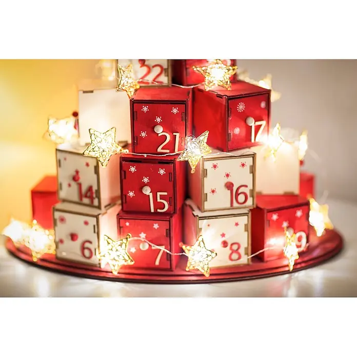 Konstsmide LED-Lichterkette - Innen, Lichtfarbe: Warmweiß, Anzahl Leuchtmittel: 20 Stk., Batteriebetrieben - Hölzerner Adventskalender mit rot-weißen nummerierten Schubladen, dekoriert mit leuchtenden Sternlichtern.
