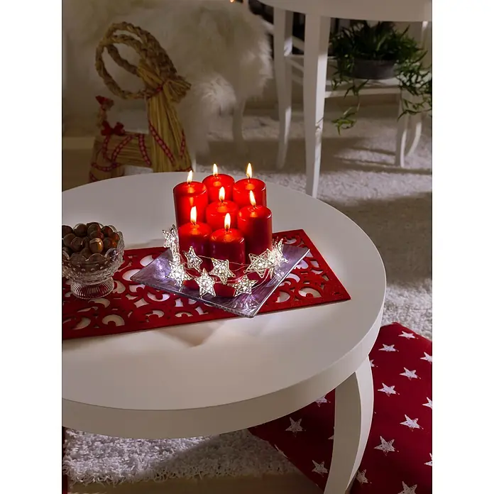Konstsmide LED-Lichterkette - Innen, Lichtfarbe: Warmweiß, Anzahl Leuchtmittel: 20 Stk., Batteriebetrieben - Festliches Arrangement mit roten Kerzen, Sternenlichtern und Nüssen auf weißem Tisch mit rotem Platzdeckchen.