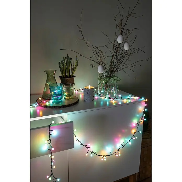 Konstsmide LED-Clusterlichterkette Globe Pastell - Außen, Länge: 4,38 m, 200 Stk., Netzbetrieben - Bunte Lichterkette über einem weißen Schrank drapiert, beleuchtet eine festliche Dekoration.