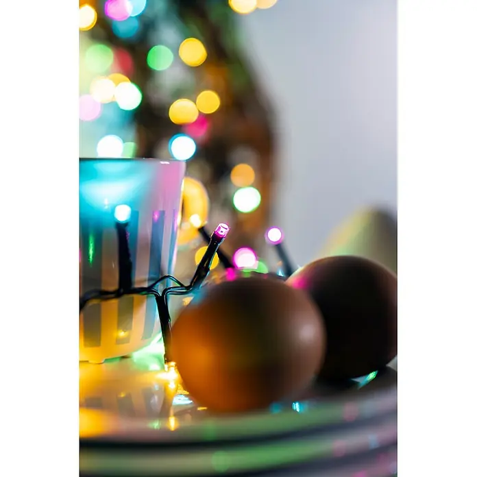 Konstsmide LED-Clusterlichterkette Pastell - Außen, Länge: 8,78 cm, 400 Stk., Netzbetrieben - Mehrfarbige LED-Lichterkette um eine Tasse gewickelt, mit zwei braunen Eiern im Vordergrund.