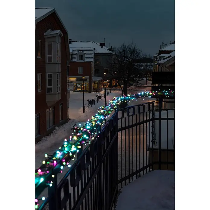 Konstsmide LED-Clusterlichterkette Pastell - Außen, Länge: 8,78 cm, 400 Stk., Netzbetrieben - Bunte Lichterketten um ein dunkles Metallgeländer gewickelt, die eine verschneite Außenansicht bei Nacht beleuchten.