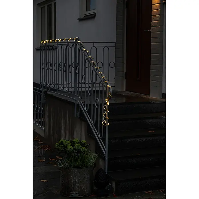 Konstsmide LED-Lichtschlauch Mini - Länge: 5 cm, Lichtfarbe: Warmweiß, 3,6 W, 392 lm, 220 V - 240 V - Warmweiße Lichterkette, um ein dunkles Metallgeländer gewickelt, beleuchtet einen Gebäudeeingang in der Dämmerung.