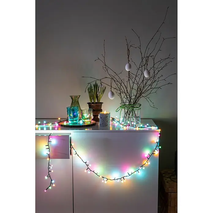 Konstsmide LED-Clusterlichterkette Globe Pastell - Außen, Länge: 8,78 cm, Netzbetrieben - Bunte LED-Lichterkette über einem weißen Schrank, beleuchtet Osterdekorationen und sorgt für festliche Stimmung.