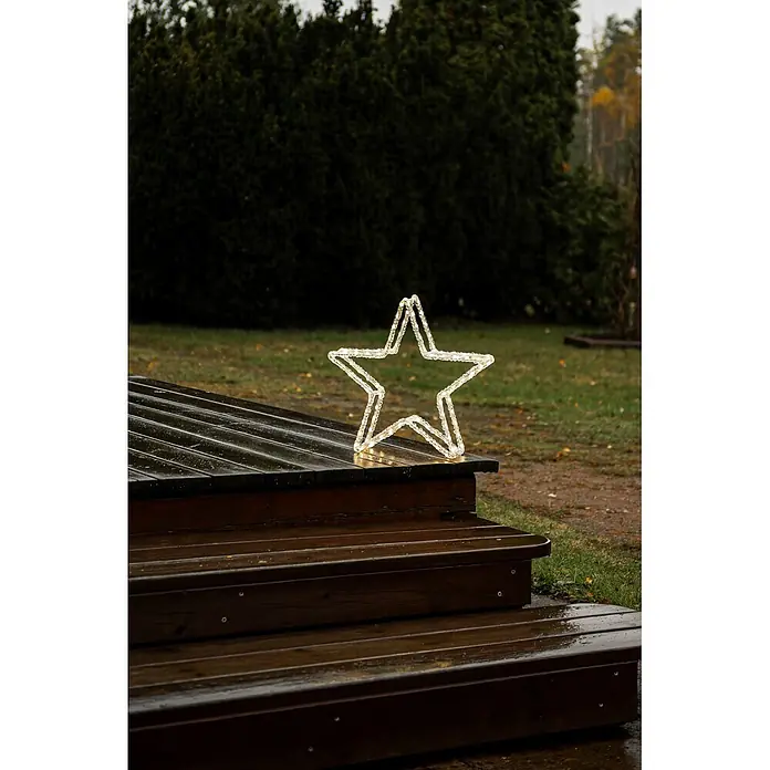 Konstsmide LED-Stern - 40 cm, Lichtfarbe: Warmweiß, IP44, Netzbetrieben - Eine weiße, beleuchtete Sterndekoration steht auf nassen Holzstufen im Freien.