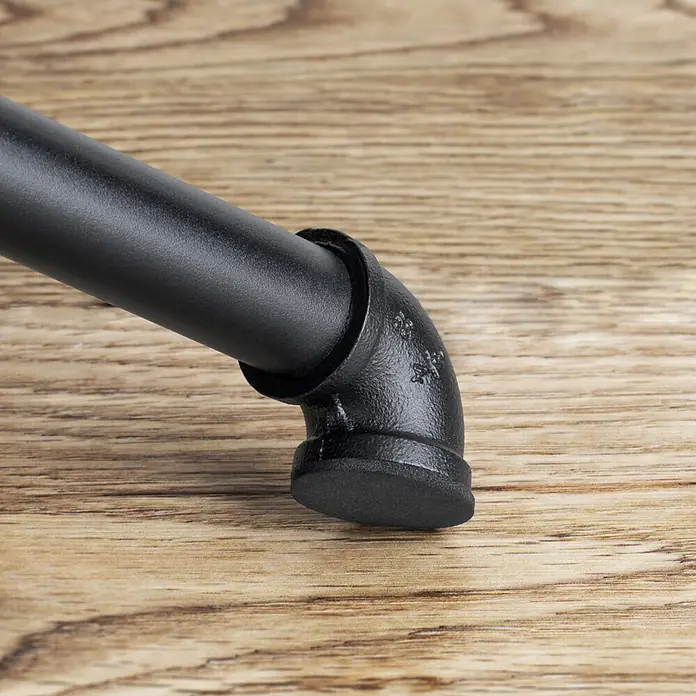 Walteco Rusticline Anti-Rutsch-Pad RT-62, Ø34mm,12STK - Durchmesser: 34 mm, Schwarz, Kleben, 12 Stk. - Schwarzes Industrie-Rohrbogenstück mit flachem Fuß, an ein Rohr angeschlossen, auf einer Holzfläche.