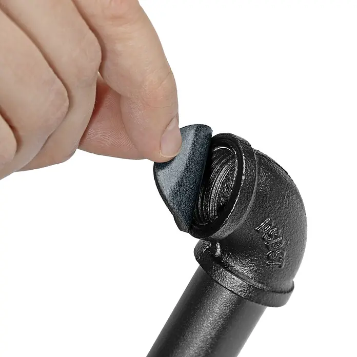 Walteco Rusticline Anti-Rutsch-Pad RT-62, Ø34mm,12STK - Durchmesser: 34 mm, Schwarz, Kleben, 12 Stk. - Eine Hand steckt ein schwarzes, weiches Polster in die Öffnung eines schwarzen Rohrbogens.