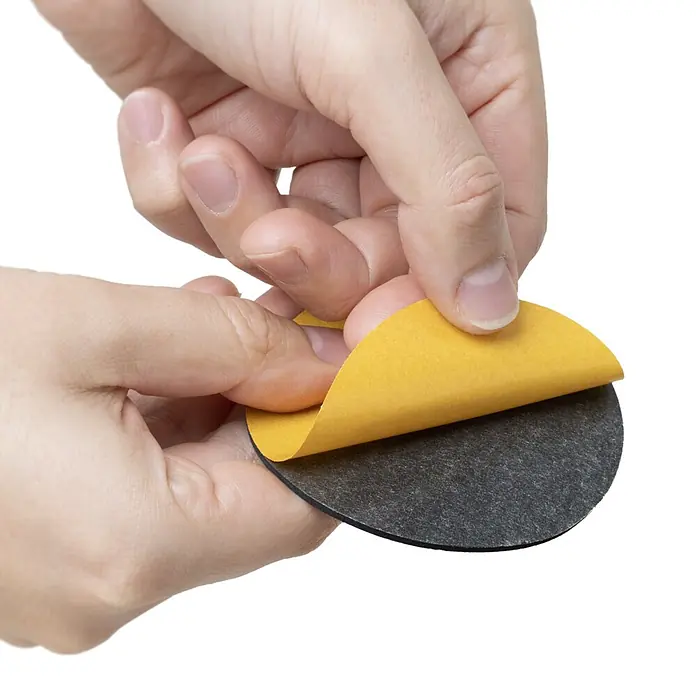 Walteco Rusticline Anti-Rutsch-Pad RT-61, Ø83mm,4STK - Durchmesser: 83 mm, Schwarz, Kleben, 4 Stk. - Hände ziehen gelbe Klebeschutzfolie von einem runden schwarzen Filzgleiter ab.