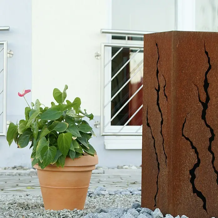 Geli Pflanzkübel rund Milano - Max. Außendurchmesser: 35 cm, Höhe: 28 cm, Terracotta - Ein Pflanzgefäß mit einer Anthurie-Pflanze steht neben einer Rostsäule mit dekorativen Rissen im Garten.