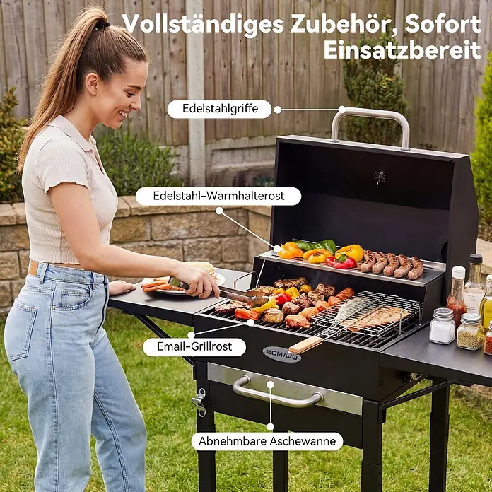 HOMAVO Holzkohlegrill - schwarz - Schwarzer BBQ-Grill mit Edelstahlgriffen, Warmhalterost, Emaille-Rost und abnehmbarer Aschewanne, in einer Gartenumgebung genutzt.