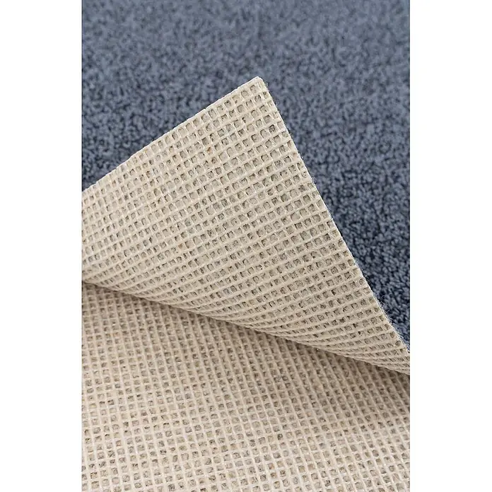 Bricoflor Teppichboden Meterware 9x4m, Schlinge meliert, dunkel-grau blau - Schlinge, 100 % Polyamid (PA), dunkel-grau blau - Blau-grauer Teppich mit beiger, gittergemusterter Anti-Rutsch-Unterlage, teilweise angehoben.