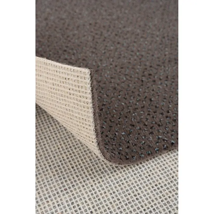 Bricoflor Teppichboden Meterware Velours gemustert, braun grau, 550 x 400 cm - Breite: 400 cm, Velours, 100 % Polyamid (PA), braun grau - Brauner Teppich, Ecke angehoben, zeigt die strukturierte Antirutsch-Rückseite auf einer beigen Antirutschmatte.