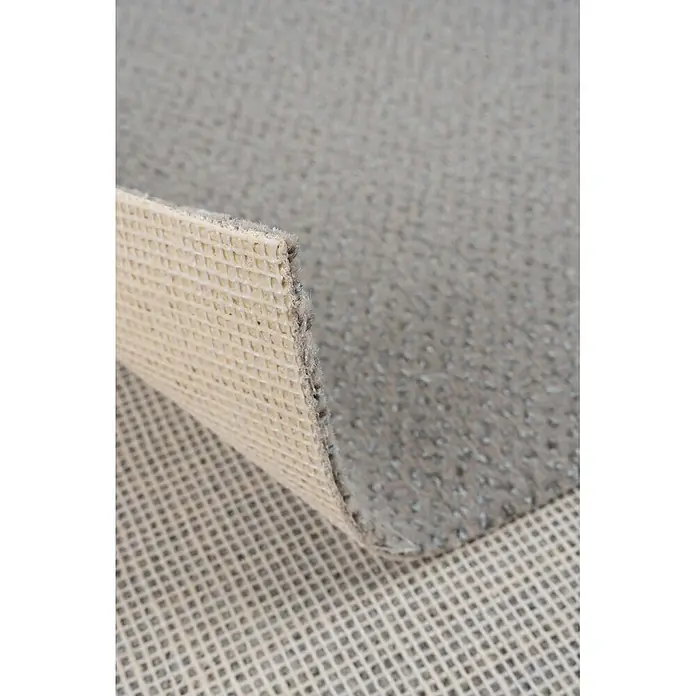 Bricoflor Teppichboden Meterware Velours gemustert, hell-grau weiß, 900 x 400 cm - Breite: 400 cm, Velours, 100 % Polyamid (PA), hell-grau weiß - Ecke eines grauen Teppichs angehoben, um die beigefarbene, gitterförmige Antirutschunterlage zu zeigen.