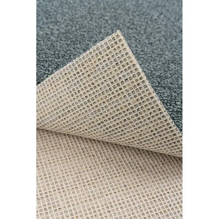 Bricoflor Teppichboden Meterware 6,5x4m, Schlinge meliert, grau blau - Schlinge, 100 % Polyamid (PA), grau blau - Nahaufnahme der teilweise umgeklappten Unterseite eines grauen Teppichs, die eine beigefarbene Gitter-Antirutschunterlage zeigt.