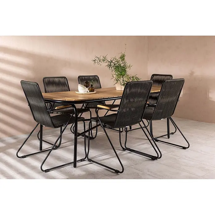 Ebuy24 Gartentisch-Set Holmbeck - Gesamtumfang: 7 -tlg., L x B x H: 90 x 200 x 75 cm, Ø x H: 90 x 75 cm, Stahl Akazie, Stapelbar - Outdoor-Essgruppe: Holztisch mit schwarzem Metallgestell und sechs Stühlen mit dunklen geflochtenen Sitzen auf einer Terrasse.