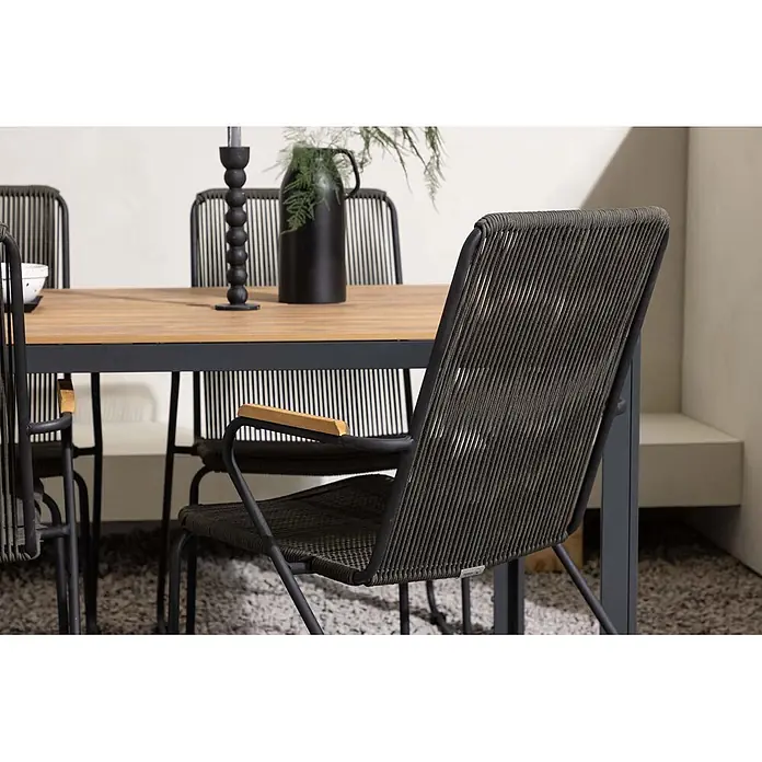Ebuy24 Gartentisch-Set Break - Gesamtumfang: 5 -tlg., L x B x H: 90 x 150 x 74 cm, Ø x H: 90 x 74 cm, Stahl Aluminum, Stapelbar - Dunkler geflochtener Outdoor-Esszimmerstuhl mit schwarzem Gestell und Holzarmlehnen, neben einem Holztisch.