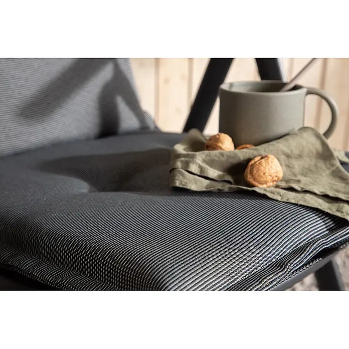 Ebuy24 Sitzauflage Cus - 1 Stk., L x B x H: 46 x 116 x 6 cm, Fasern, Schaum, Polyester., Hellgrau - Gestreiftes, gepolstertes Stuhlkissen in Dunkelgrau und Weiß auf einem Stuhl in gemütlicher Umgebung mit Tasse und Walnüssen.