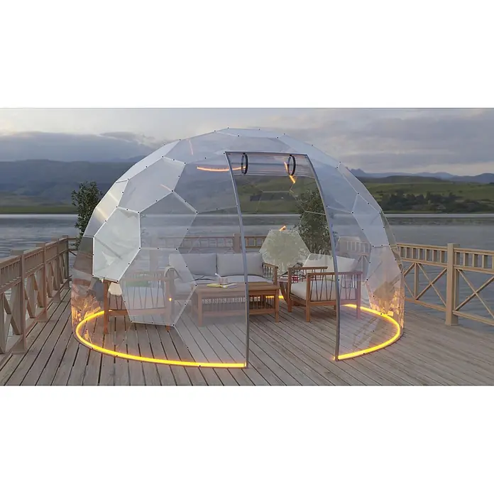 BubbleOrb Gartenkuppel - Durchmesser: 360 cm, Transparent - Ein transparenter geodätischer Dom mit orangefarbener LED-Beleuchtung am Boden, als Outdoor-Lounge mit Holzmöbeln auf einer Seeterrasse.