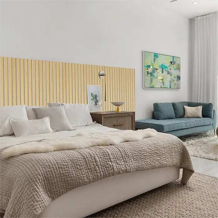 Sonido Akustikpaneel - New Oak Light / beiger Filz, 1.200 x 560 x 18 mm - Ein modernes Schlafzimmer mit einem Bett mit taupefarbenem Steppbett und weißen Kissen vor einer hellen Holzlamellen-Kopfteil, daneben eine blaue Chaiselongue.
