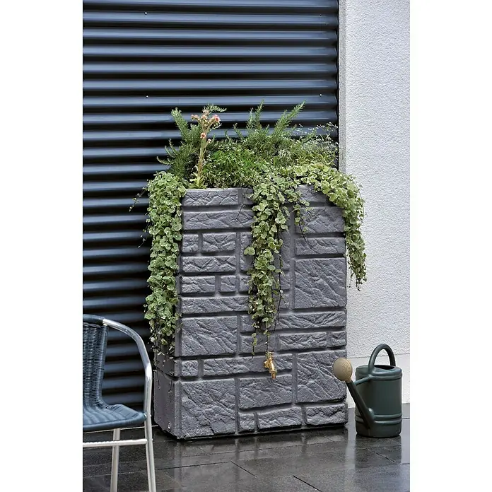 Arves Regenspeicher Maurano - 300 l, Black Granitfarben, 1 Stk. - Ein grauer, steinerner Regenwassertank mit Pflanzen darauf, eine Gießkanne steht daneben.