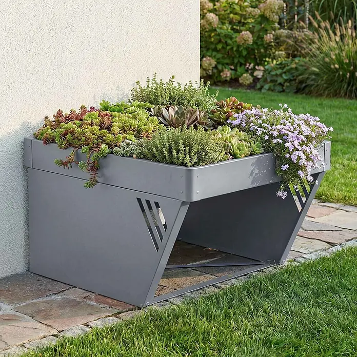Proregal Mähroboter-Garage Mit Pflanzkasten - L x B x H: 70 x 60 x 40 cm, Grau, Ausführungseigenschaft: mit Pultdach, Gardena, WORX, Husqvarna, Einhell, Landxcape, Juka - Graues Metall-Pflanzgefäß mit angewinkeltem Sockel, Sukkulenten und kleinen Blumen, außen an einer Wand platziert.