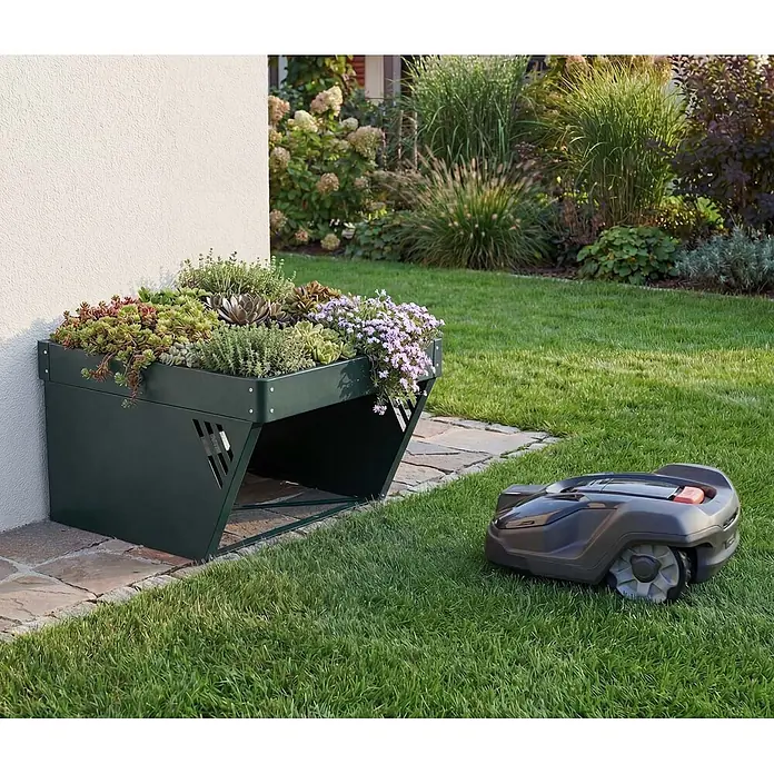 Proregal Mähroboter-Garage Mit Pflanzkasten - L x B x H: 70 x 60 x 40 cm, Grün, Ausführungseigenschaft: mit Pultdach, Gardena, WORX, Husqvarna, Einhell, Landxcape, Juka - Dunkelgrüne Mähroboter-Garage mit bepflanztem Dach aus Sukkulenten und Blumen, neben einem Rasenmäher.