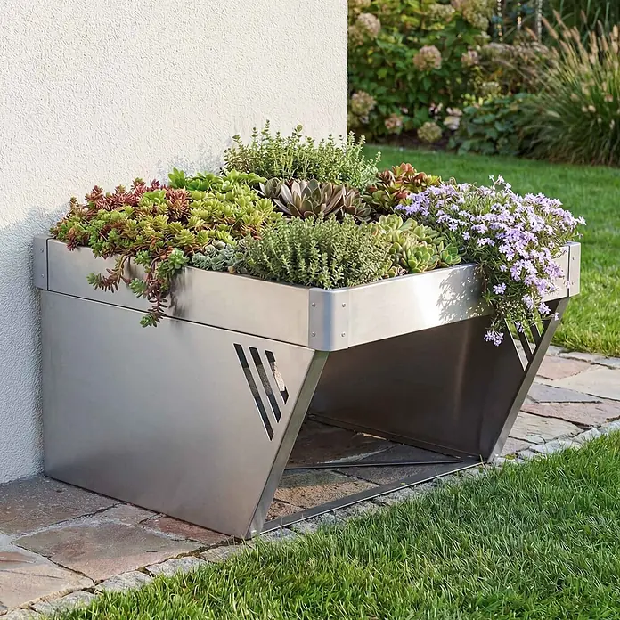 Proregal Mähroboter-Garage Mit Pflanzkasten - L x B x H: 70 x 60 x 40 cm, Silber, Ausführungseigenschaft: mit Pultdach, Gardena, WORX, Husqvarna, Einhell, Landxcape, Juka - Ein eleganter, schräger Edelstahl-Pflanzkasten gefüllt mit Sukkulenten und Blütenpflanzen, draußen an einer strukturierten Wand.