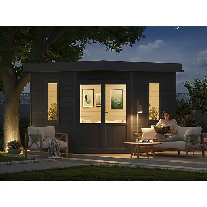 Fjordholz Gartenhaus Style Classic - Außenmaß inkl. Dachüberstand (B x T): 336 x 336 cm, Aluminium, Anthrazit/grau - Modernes schwarzes Gartenhaus bei Nacht mit einer Frau, die auf einer Terrasse mit Gartenmöbeln im sanften Licht liest.
