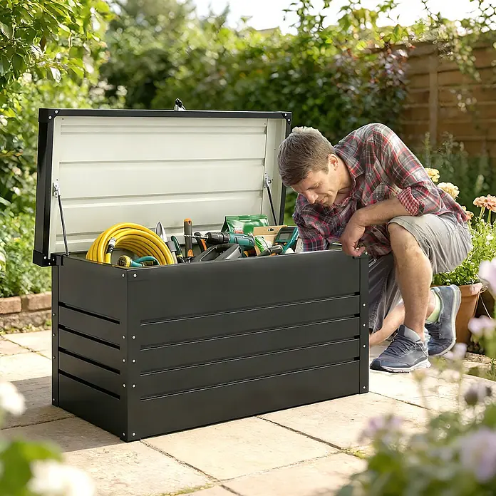 Outsunny Garten-Aufbewahrungsbox - Grau, Stahl - Dunkelgraue Gartenaufbewahrungsbox, aus der ein Mann Werkzeuge entnimmt. Sie enthält Gartenschläuche, Bohrer und diverse Gartengeräte.