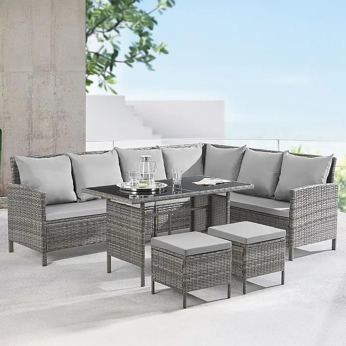 SVITA Loungemöbel-Set MADISON - 6 -tlg., Polyrattan, pulverbeschichteter Stahl, Variabel stellbar, Grau - Graues Rattan-L-förmiges Gartensofa-Set mit schwarzem Glastisch und zwei Hockern, alle mit hellgrauen Kissen, auf einer Terrasse.